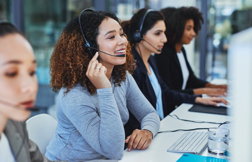 Image of a woman in a call center in front of computer and talking into headset.